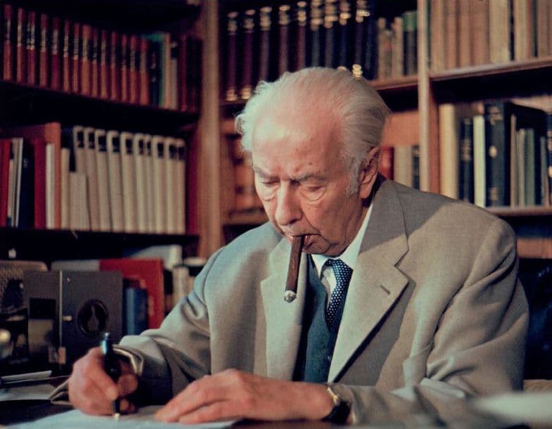 Symbolfoto für die Themenführung. Theodor Heuss sitzt an seinem Schreibtisch und schreibt. Er raucht Zigarre.