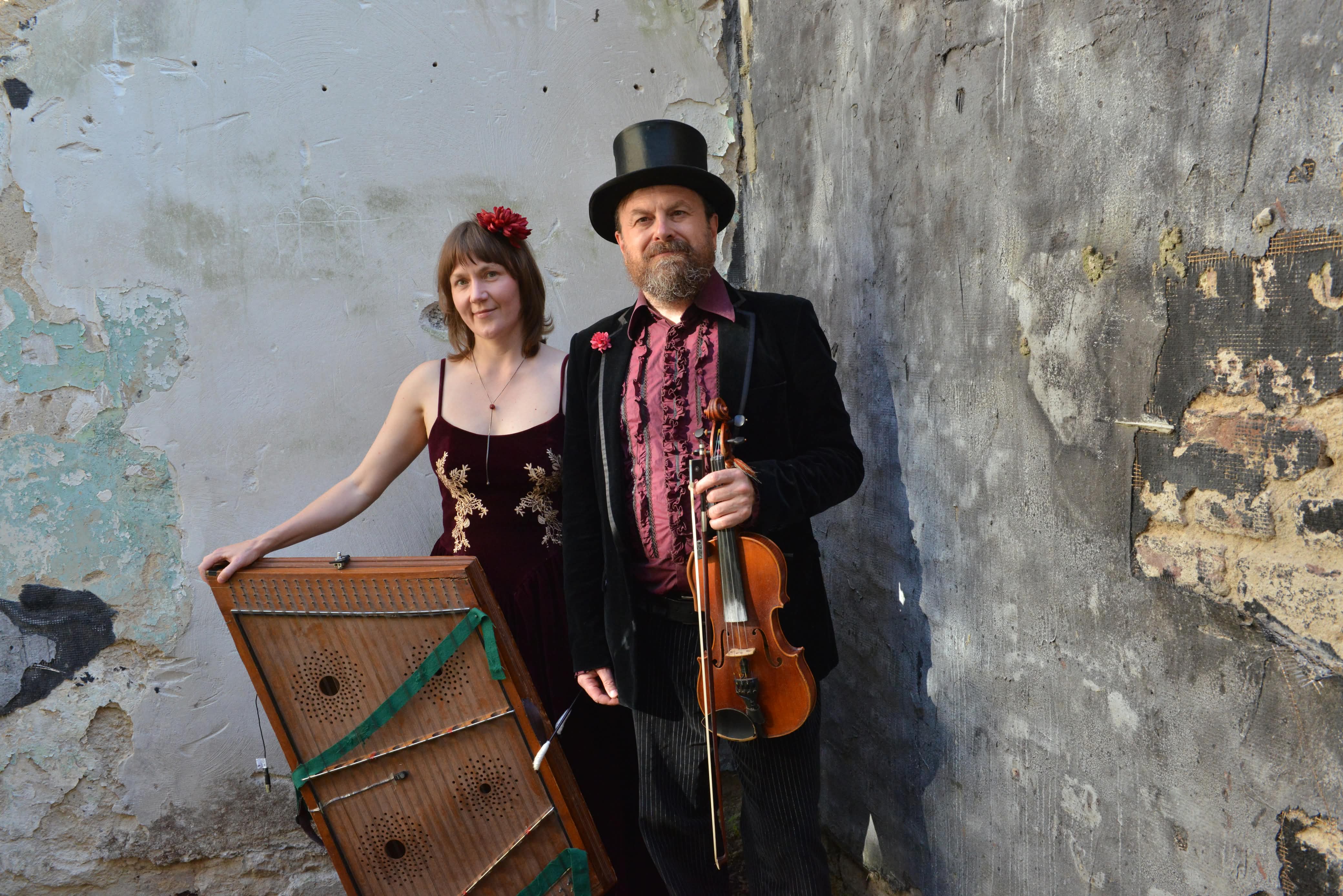 Dobranotch Duo: Eine Musikerin mit einem Hackbrett und ein Musiker mit Violine vor einer Wand.