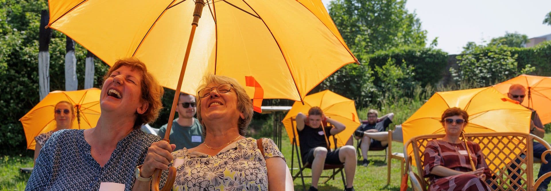 lachende Menschen im Grünen mit gelben Regenschirmen